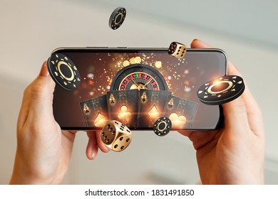 Creative background, online casino, in a man's hand a smartphone with playing cards, roulette and chips, black-gold background. Internet gambling concept. Copy space. - Shutterstock ID 1831491850