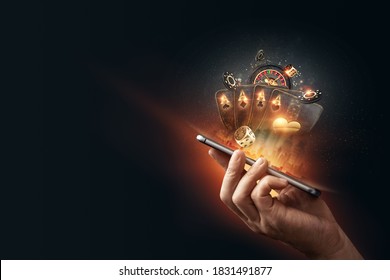 Creative background, online casino, in a man's hand a smartphone with playing cards, roulette and chips, black-gold background. Internet gambling concept. Copy space.