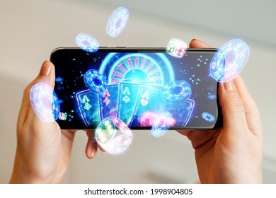 Creative background, online casino, in a man's hand a smartphone with playing cards, roulette and chips, black-neon background. Internet gambling concept. Copy space - Shutterstock ID 1998904805
