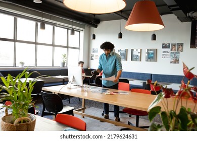 Creative Biracial Young Businessman With Camera And Photograph At Computer Desk In Office. Unaltered, Creative Business, Workplace, Photography Themes.