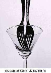 Creative black and white composition of a fork placed inside a glass, creating reflections and distortion, forming an abstract minimal still life.