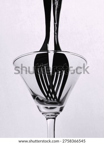 Creative black and white composition of a fork placed inside a glass, creating reflections and distortion, forming an abstract minimal still life.