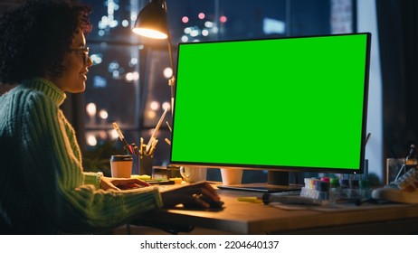 Creative Black Woman Sitting at Her Desk, Using Desktop Computer with Mock-up Green Screen Chromakey. Female Specialist Using Mouse, Scrolling Through Objects, Adding New Elements. Freelance Concept. - Powered by Shutterstock