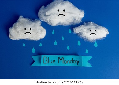 Creative Blue Monday composition featuring cotton clouds with sad faces, paper rain drops, and a banner on a blue background.