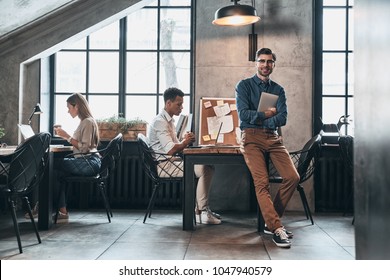 Creative Business. Handsome Young Man In Smart Casual Wear Smiling While Spending Time In The Office With His Coworkers