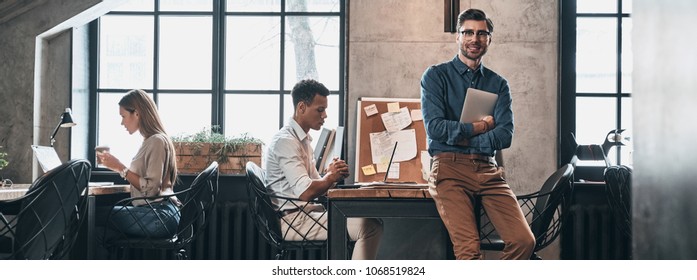 Creative business. Handsome young man in smart casual wear smiling while spending time in the office with his coworkers - Shutterstock ID 1068519824