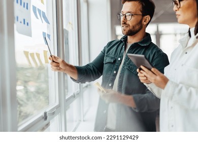 Creative business people brainstorming with sticky notes in an office. Business professionals standing next to a window and discussing their ideas. - Powered by Shutterstock