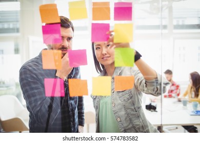 Creative Business People Looking At Multi Colored Sticky Notes On Glass In Meeting Room At Creative Office