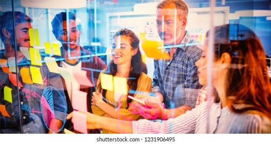 Creative business team looking at sticky notes on glass window in office - Powered by Shutterstock