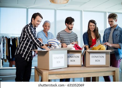 Creative Business Team Sorting Clothes In Donation Box In Office