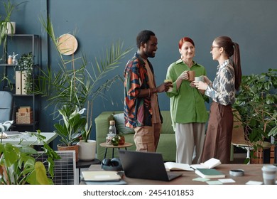 Creative business team of three people communicating standing in modern office at coffee break against blue wall copy space - Powered by Shutterstock