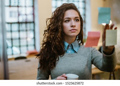 Creative Businesswoman Analyzing Papers Stuck On Wall In Office.