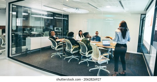 Creative businesswoman giving a presentation in a boardroom. Confident businesswoman presenting financial data to her colleagues in a modern workplace. Group of businesspeople attending a briefing. - Powered by Shutterstock