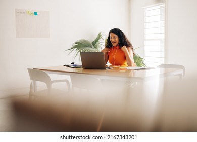 Creative Businesswoman Smiling Excitedly During An Online Meeting Her Business Partners. Cheerful Young Businesswoman Having A Video Call In A Modern Boardroom.