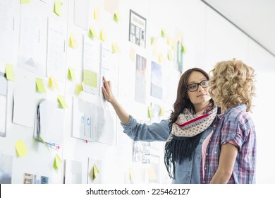 Creative Businesswomen Discussing Over Papers Stuck On Wall In Office