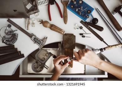 Creative chaos. Top view of jeweler's workbench with different tools for making jewelry. Female jeweler's hands polishing a silver ring
