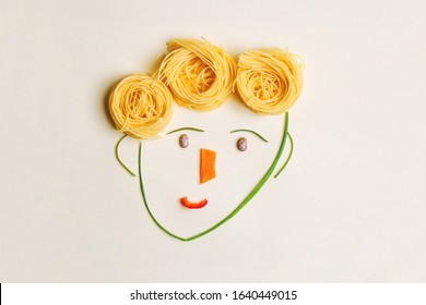 creative children food concept, cute boy's face made of ripe vegetables and Italian spaghetti pasta as hair, flat lay, top view