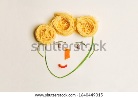 creative children food concept, cute boy's face made of ripe vegetables and Italian spaghetti pasta as hair, flat lay, top view