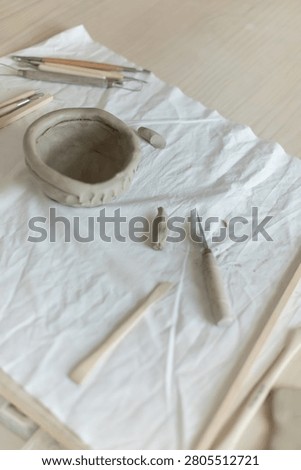 Creative clay pot on worktable with wooden handles and cloth, top-down perspective, gray and white tones, artistic and serene mood, crafting and pottery context.