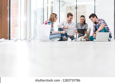 Creative colleagues discussing while sitting on floor in office