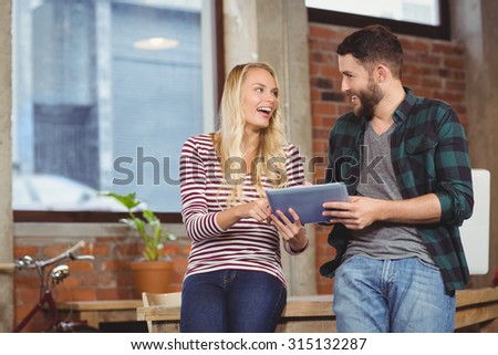 Creative colleagues smiling while discussing over tablet in creative ofice