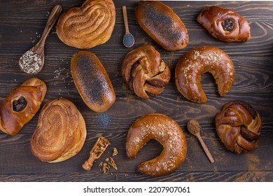 Creative composition of different buns, many sweet buns on a dark wooden background: poppy seed bun, cinnamon bun, jam bun. Advertisement, catalog for a bakery. Flat lay, pattern