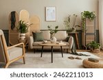 Creative composition of living room interior with beige sofa, wooden coffee table, rattan sideboard, partition wall, lamp, beige carpet, stylish armchair and personal accessories. Home decor. Template