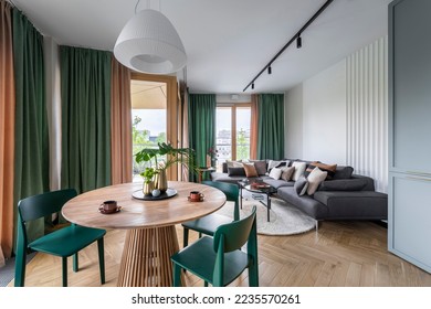 Creative composition of living room interior with dinning room, round table, green chairs, modern sofa, coffee table, beige rug, curtain, vase with leaves, pillows and accessories. Home decor. 