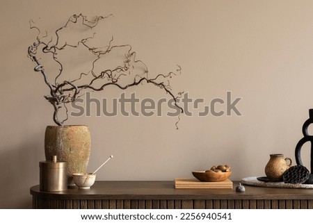 Creative composition of living room interior with wooden sideboard, stylish vase with branch, stylish casket, books, nuts in bowl, brown wall and personal accessories. Home decor. Template. 
