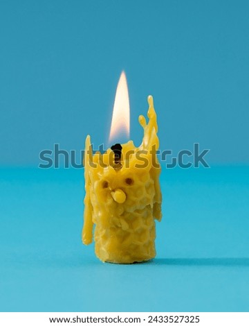 Creative composition made with burnt out yellow beeswax candle melting and creating silly funny face on blue background. Minimal timeline concept. Trendy beeswax candle idea.