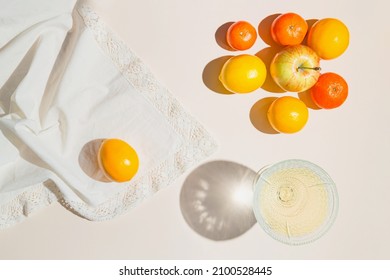 Creative composition made of glass with fruit juice, lemon, mandarin and apples on pastel beige sunlit background with white cloth and shadows. Summer and refreshment concept. Harvest theme