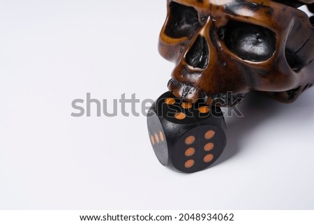 Creative composition of a skull and a dice, a skull bites a dice, on a white background, space for copying, Dramatic concept.