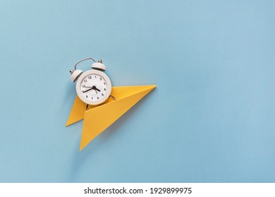 Creative composition Time flies. A small white alarm clock on a yellow paper on a paper blue background. Top view. Flat lay.