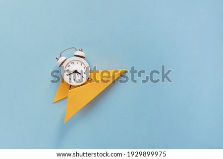 Creative composition Time flies. A small white alarm clock on a yellow paper on a paper blue background. Top view. Flat lay.