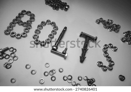 Creative composition of the word BOLTS made from hardware fasteners. Industrial background with scattered steel nuts, screws, and wall plugs on flat white surface.