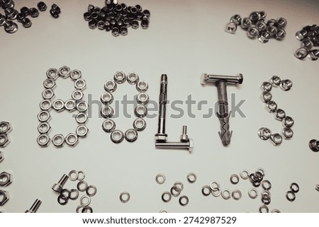 Creative composition of the word BOLTS made from hardware fasteners. Industrial background with scattered steel nuts, screws, and wall plugs on flat white surface.