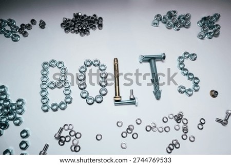Creative composition of the word BOLTS made from hardware fasteners. Industrial background with scattered steel nuts, screws, and wall plugs on flat white surface.