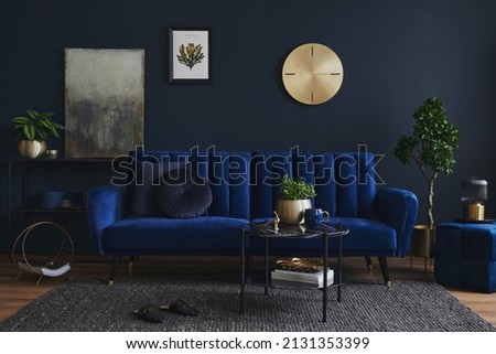 Creative compositon of modern living room interior design with glamour blue sofa, metal shelf, coffee table and elegant home accessories. Dark blue wall. Home staging. Template. Copy space.