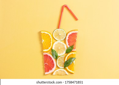 Creative concept of citrus juice, smoothie, summer drinks. Slices of orange, grapefruit, lemon and lime are folded in the shape of glass on yellow background. Top - red, yellow, green, orange tubules.