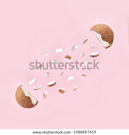 Creative concept of the fresh, organic coconut cut in half with small pieces. 
Healthy fruit explosion on pastel  pink background.