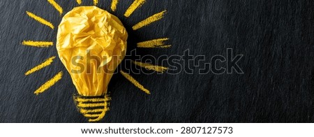 A creative concept image featuring a crumpled yellow light bulb with sunburst rays against a dark, textured surface, representing innovation and inspiration.