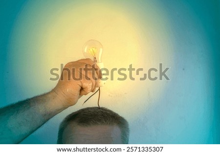 Creative concept image of a hand holding a glowing light bulb above a person's head, symbolizing a bright idea or innovation.