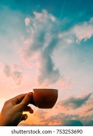 Creative Concept Of Man Holding Coffe Cup In Front Of Sunset Clouds