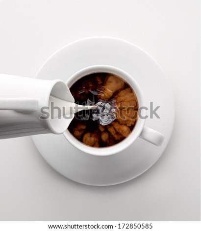 Creative concept photo of jar pouring refreshment drink beverage liquid milk in a white cup mug of coffee on grey background.