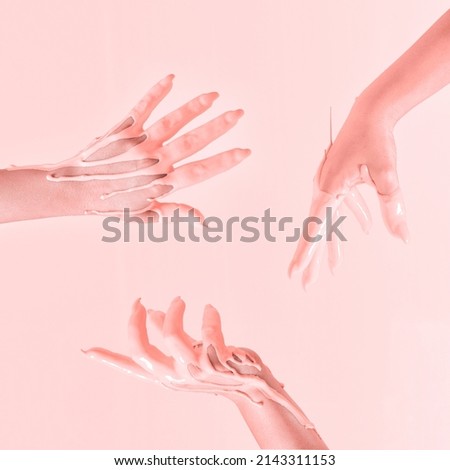 Creative concept of a raised hands dipped in peachy paint in the air. Pastel pink background.