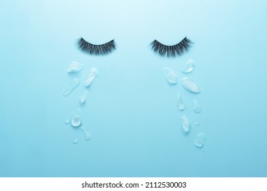 Creative concept of sadness. Glued lashes on a blue background with tears in the form of ice pieces.  