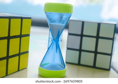 Creative concept of time and intelligence featuring an hourglass between two Rubik cubes on a clean background, symbolizing patience, focus, and problem solving.