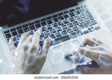 Creative concept of wireless technology with hexagon hologram and hands typing on laptop on background. Big data and database concept. Multiexposure