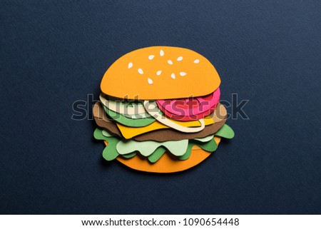 Creative conceptual minimal art collage. Paper craft hamburger with cheese tomatoes and onions on a blue background. Composition cut out from colored paper. Illustrative close-up picture. 