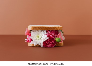 The creative conceptual sandwich is made with various flowers on the pastel background. Minimal summer food theme.